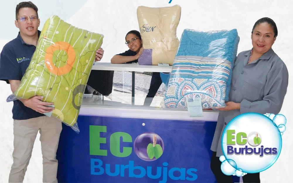 Tres integrantes del equipo sonríen con edredones junto al mostrador de EcoBurbujas